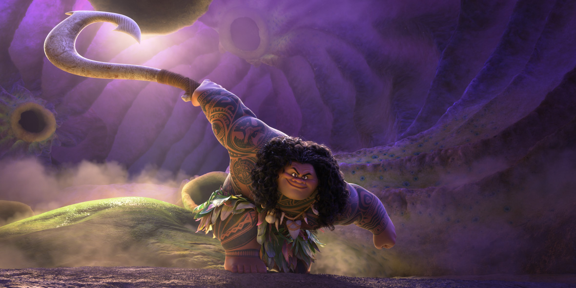 In an image from Walt Disney Animation Studios’ Moana 2, Maui (voiced by Dwayne Johnson) has just landed from a jump, knelling on one knee with his right arm extended, brandishing his hook. He is in a purple cave filled with fog.