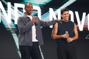 Captain America: Brave New World stars Anthony Mackie (left), who makes his big-screen debut as Captain America, and Danny Ramirez (right), who plays the Falcon, appear together onstage to talk about the film, which releases in theaters on February 14, 2025. Behind them is a huge video display showing what appear to be falling stars.