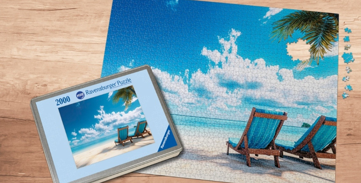 A Dual image showcasing Ravensburger Custom Photo Puzzle product, shows a large image of a puzzle featuring an image of two blue beach loungers from back on the sand with an ocean with sunny blue sky and puffy clouds, with the top of a palm tree at upper left and the puzzle box for the image smaller and embedded at lower left.