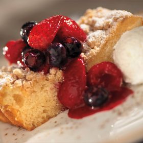 An image of a slice of buttermilk cake with berry compote and a scoop of vanilla ice cream on the side.