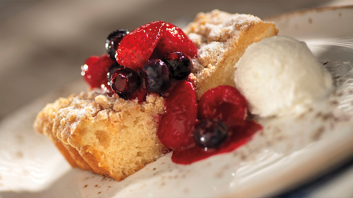 An image of a slice of buttermilk cake with berry compote and a scoop of vanilla ice cream on the side.