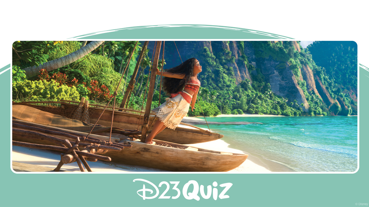 In an image from Moana, Moana (voiced by Auli&rsquo;i Cravalho) stands confidently at the stern of a wooden canoe, gripping the central mast with her right hand as she leans forward. She wears a red crop top with intricate patterns paired with a white wrap skirt accented by dark yellow details. The background showcases lush green mountains, a shoreline, and sparkling crystal-clear waters.