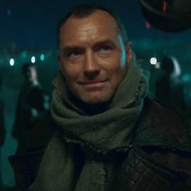 In an image from Star Wars: Skeleton Crew, Jod Na Nawood (Jude Law) is closely examined by security droid eyestalks. He wears a black leather jacket and a gray shawl around his neck. His young partners stand in the background, which features a clear night sky and terrain.