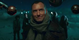 In an image from Star Wars: Skeleton Crew, Jod Na Nawood (Jude Law) is closely examined by security droid eyestalks. He wears a black leather jacket and a gray shawl around his neck. His young partners stand in the background, which features a clear night sky and terrain.
