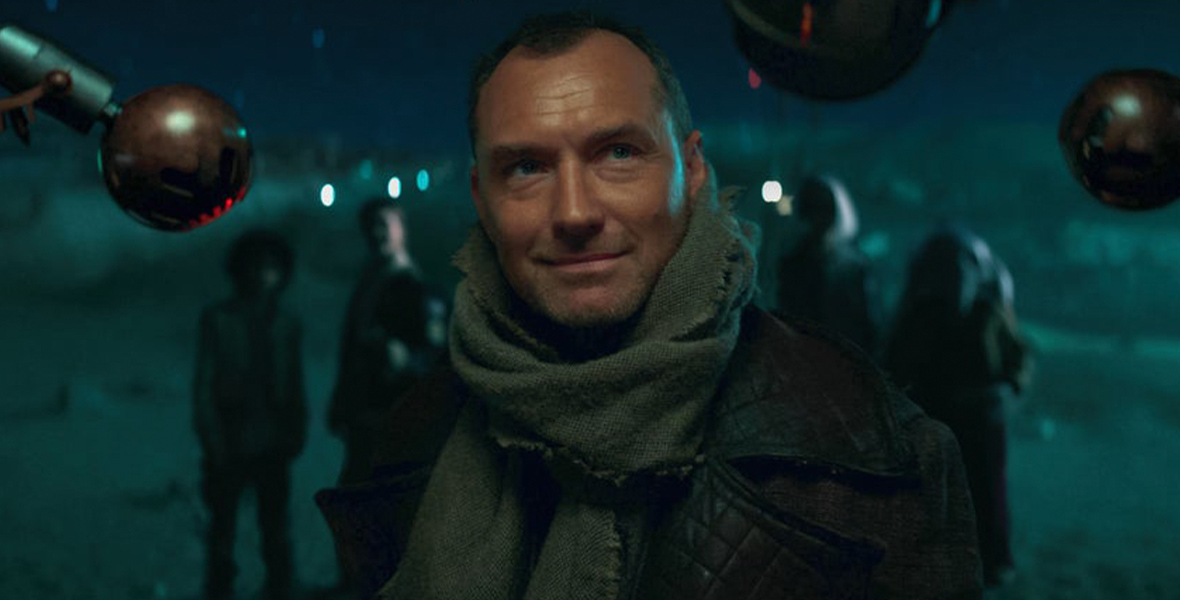 In an image from Star Wars: Skeleton Crew, Jod Na Nawood (Jude Law) is closely examined by security droid eyestalks. He wears a black leather jacket and a gray shawl around his neck. His young partners stand in the background, which features a clear night sky and terrain.