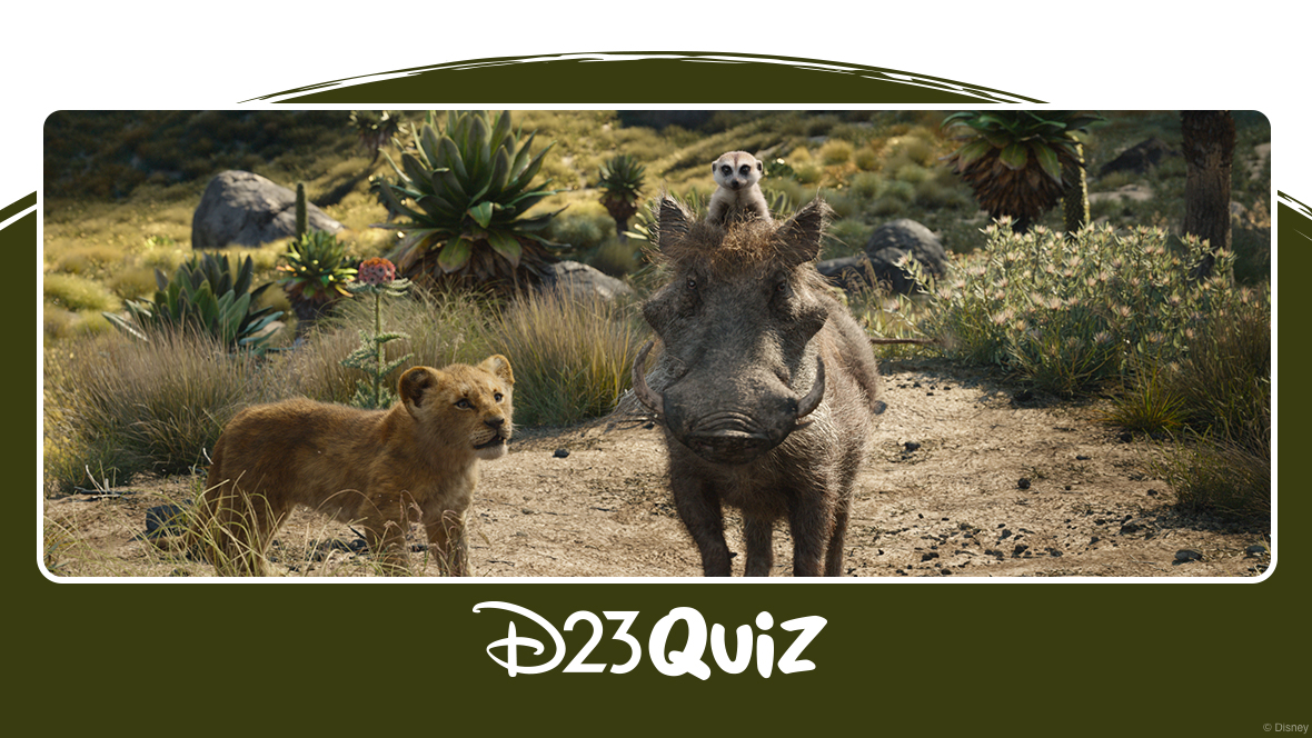 In an image from The Lion King (2019), young Simba (voiced by JD McCrary), a lion cub, walks alongside Pumbaa (voiced by Seth Rogen), a warthog, and Timon (voiced by Billy Eichner), a meerkat perched on Pumbaa's head. The background features rocky terrain, trees, and flowers, with the trio standing on dry, barren ground. In the distance, the landscape becomes lusher and more vibrant.