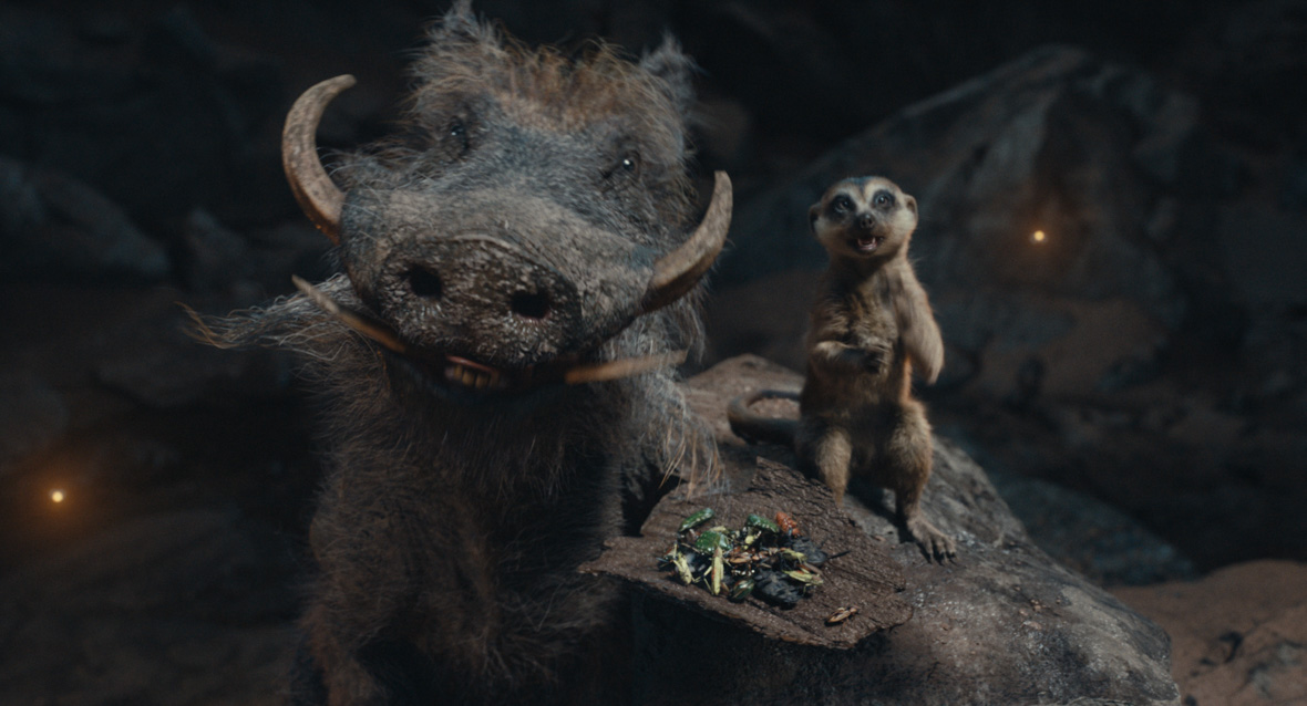 (L-R): Pumbaa (voiced by Seth Rogen) and Timon (voiced by Billy Eichner) in Disney’s live-action Mufasa: The Lion King. They are both smiling at the camera. A plate of bugs is resting on Pumbaa.