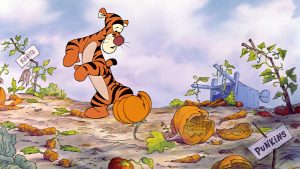 In an image from the animated film Winnie the Pooh and Tigger Too, Tigger stands in a ruined vegetable garden. He has a worried look on his face as he looks down at his feet, one of which is stuck in a broken clay pot. Around him on the ground are broken carrots and pumpkins and two sticks that have paper labels attached at the top, one for carrots and one for pumpkins, both of which are misspelled.