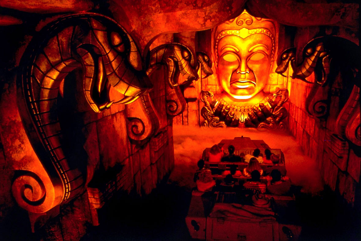 Inside of the Indiana Jones Adventure attraction at Disneyland Resort, we see five large snakes and the face of the idol looking down on a ride vehicle full of passengers. 