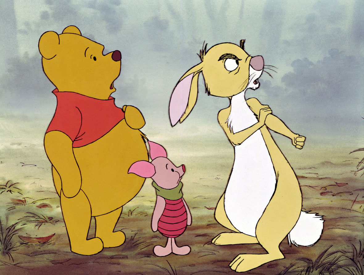 In an image from Winnie the Pooh and Tigger Too we see, from left to right, Pooh, Piglet, and Rabbit. They are standing on grass and all are looking off-screen to the right, Rabbit looks angry and appears to be rolling up an imaginary sleeve, as if he’s going to punch someone.