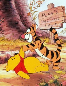 In an image from Winnie the Pooh and Tigger Too, Pooh lies on the ground, his left arm extended as he shakes hands with Tigger, who is standing at Pooh&rsquo;s feet. Pooh lies next to a log and behind them is the base of a tree and a sign reading, Pooh&rsquo;s Thoughtful Spot, with the word &ldquo;thoughtful&rdquo; misspelled.