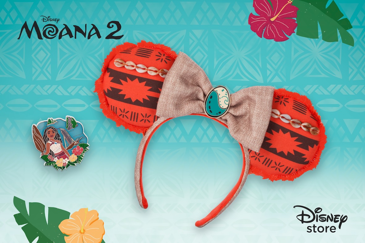 Promotional image for Moana 2 merchandise from the Disney Store, featuring a themed Minnie Mouse ear headband inspired by the film. The ears have a red and black Polynesian pattern with decorative cowrie shells along the top and a frayed red fabric trim. A beige fabric bow sits in the center, adorned with an oval emblem featuring an ocean wave design. In the lower left corner, there is an enamel pin of Moana holding the Heart of Te Fiti, surrounded by tropical flowers and a Polynesian island backdrop. The background is a bright turquoise with tribal patterns, hibiscus flowers, and tropical leaves. The 'Moana 2' logo is displayed at the top left, and the 'Disney Store' logo appears in the bottom right corner.