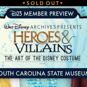 Promotional image for the D23 Member Preview of Heroes & Villains: The Art of the Disney Costume exhibit, presented by the Walt Disney Archives at the South Carolina State Museum. The design prominently features two iconic costumes from 2017s Beauty and the Beast: on the left, a detailed golden ball gown - Belle's dress, accessorized with a delicate gold necklace featuring a rose pendant; and on the right, Gaston’s red hunting suit, a rich red coat with intricate buttons and a white cravat, evoking historical attire often associated with classic Disney villains or heroes. The exhibit title is centered on a light blue textured background resembling fabric. A banner at the top reads SOLD OUT.