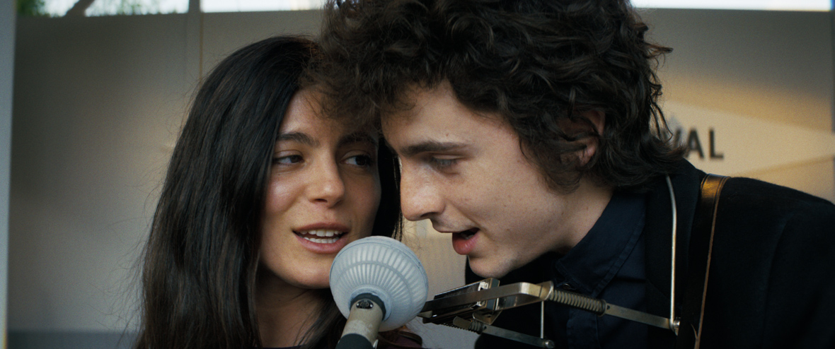 Timothée Chalamet as musician Bob Dylan and Monica Barbaro as musician Joan Baez in A Complete Unknown. They are looking at each other while singing into the same microphone.