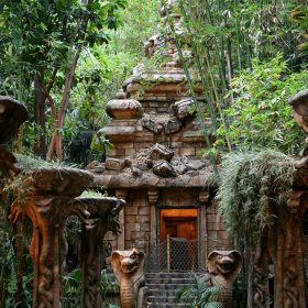 Outside queue of the Indiana Jones Adventure attraction at the Disneyland Resort. Green foliage and tall columns are seen in front of a brown stone temple, guarded by two snake statues.