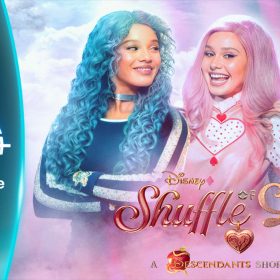 Disney+ graphic featuring three characters from Descendants all looking at each other. Chloe has blue hair and is wearing a blue long-sleeve shirt, Bridget has pink hair and is wearing a pink dress with a white and red short-sleeve shirt underneath, and Red has red hair and is wearing a red long-sleeve shirt with back hearts. Underneath the three characters reads “Shuffle of Love: A Descendants Short Story.”