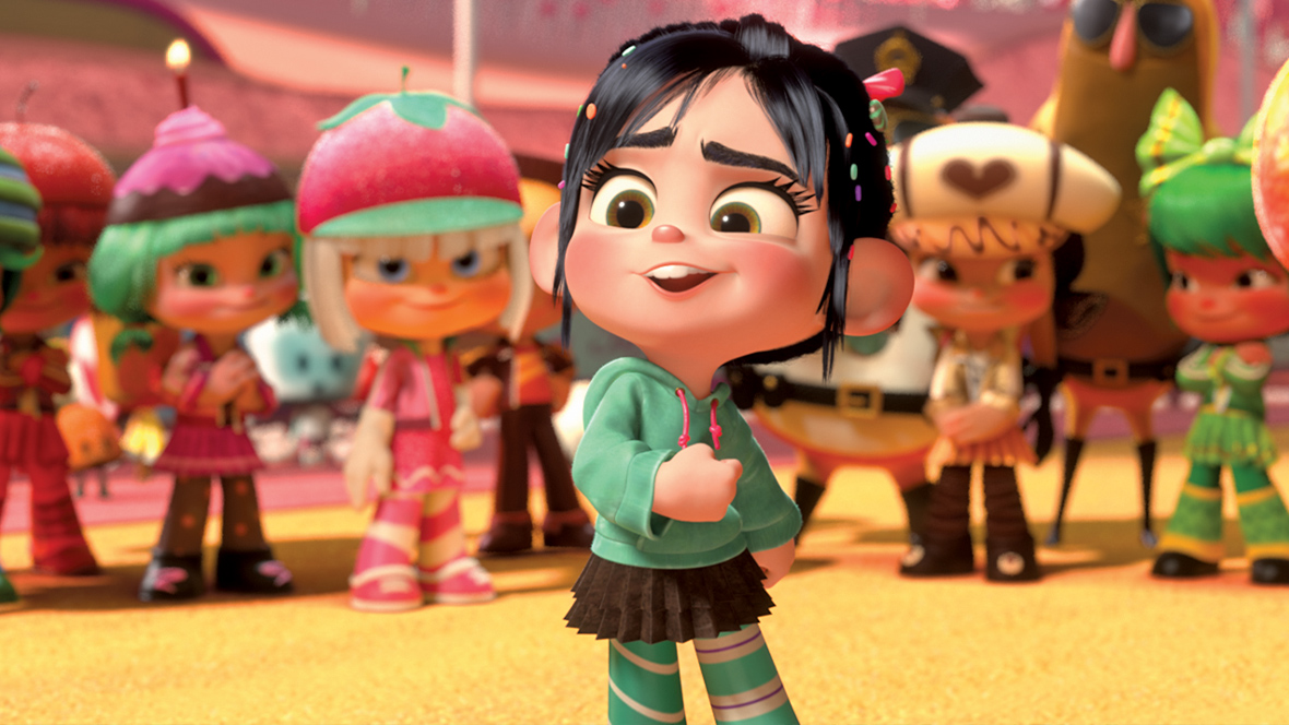 Screengrab of a scene from Wreck-It-Ralph featuring Vanellope von Schweetz in the foreground. Behind her are 10 Sugar Rush racers, and two police-donuts sent by King Candy. Vanellope is bending her right arm at chest level, and is wearing a lime-green hoodie and a brown skirt. The racers are dressed in a variety of candy-themed outfits, including an orange pumpkin, hot-pink strawberry, and a purple gumdrop."