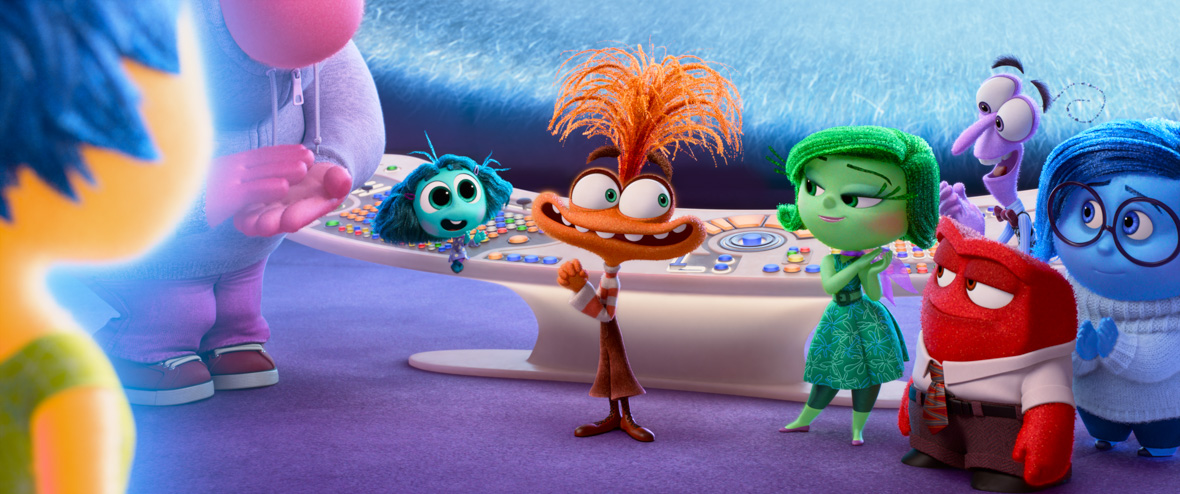 Image of the characters from Inside Out 2 in front of the control panel in Riley’s mind. The characters of Joy, Disgust, Anger, Fear, Sadness, Joy, Embarrassment and Envy all looking at the character of Anxiety in the center of the image.