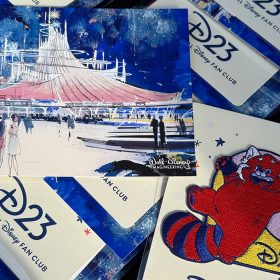 Close-up photo of the event gifts from the D23 Spotlight Series & Walt Disney Imagineering Present Space Mountain and Beyond event— a postcard of Space Mountain concept art, and a D23 Turning Red patch. The items are set on top of rows of the same gift pairings.