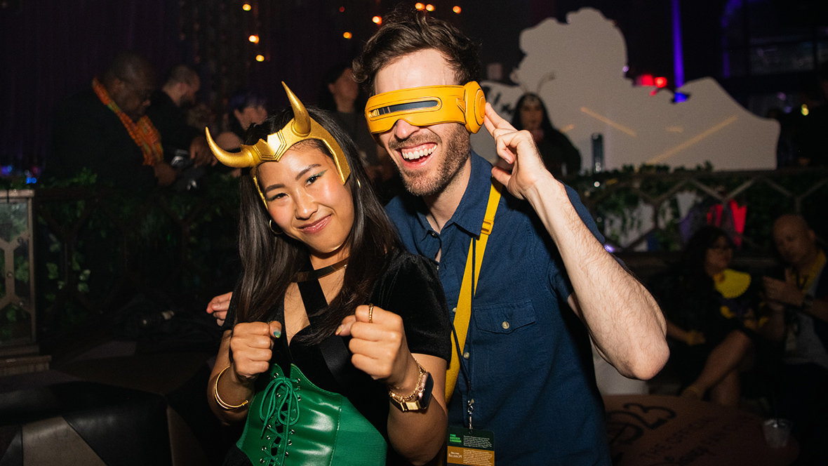 Hellfire Gala Two D23 members dressed in Marvel-inspired cosplay—one as Lady Loki and the other as Cyclops from X-Men—pose and smile at a nighttime Disney fan event, surrounded by other attendees in costume.