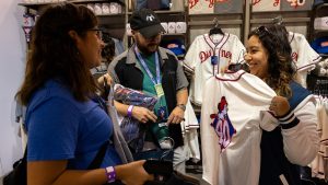 D23 members shop and chat at an exclusive merchandise booth featuring vintage-style Disney baseball jerseys, hats, and apparel celebrating the 40th anniversary of The Walt Disney Studios.
