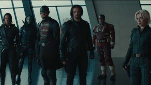 Members of the Thunderbolts* in a gray room with large windows behind them. From left to right: Ava Starr (Ghost), Antonia Dreykov (Taskmaster), John Walker (U.S. Agent), Bucky Barnes (Winter Soldier), Alexei Shostakov (Red Guardian), and Yelena Belova.