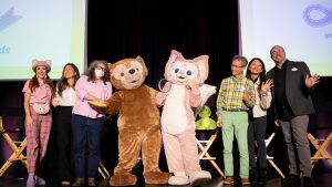 From left to right, D23’s Jessica McDonald, WDI’s Eva Lee, Laura West, Charlie Watanabe, Xiao Qing Chen, and Disney Live Entertainment’s Trevor Rush pose onstage with Duffy and LinaBell performers.