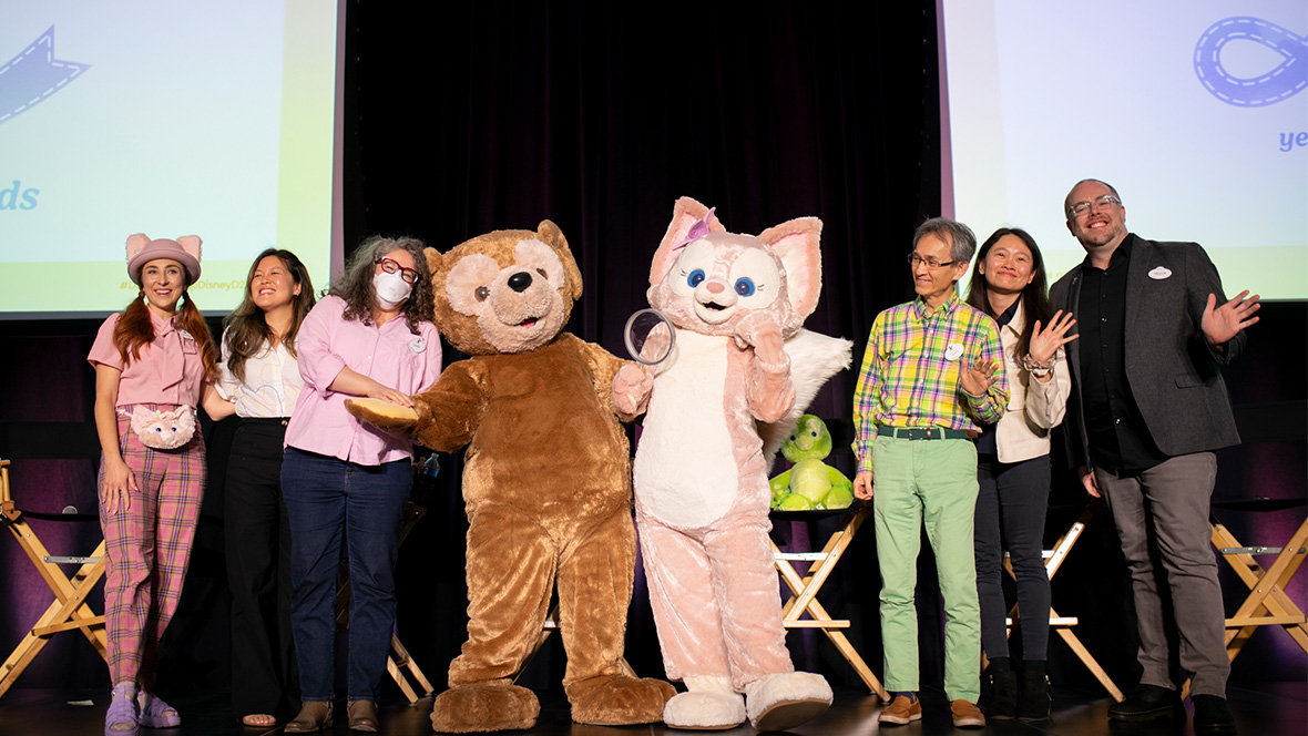 From left to right, D23’s Jessica McDonald, WDI’s Eva Lee, Laura West, Charlie Watanabe, Xiao Qing Chen, and Disney Live Entertainment’s Trevor Rush pose onstage with Duffy and LinaBell performers.