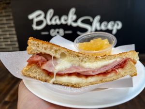 An Ohana Grilled Cheese from Black Sheep Grilled Cheese Bar, Includes melty mozzarella, honey ham, and bacon on buttery grilled bread served with a side of house-made pineapple preserves.