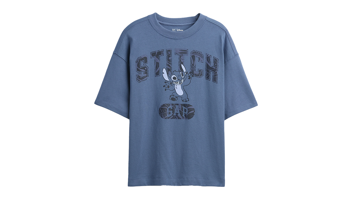 A blue GAP T-Shirt with a graphic of Stitch standing and waving overlaying bold text stating “STITCH.”