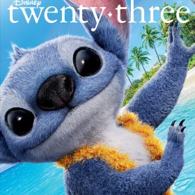 Stitch smiles playfully in a close-up shot on the beach, wearing a fluffy yellow lei, with bright blue ocean water and palm trees in the background. The image is the cover of the Summer 2025 issue of Disney twenty-three.
