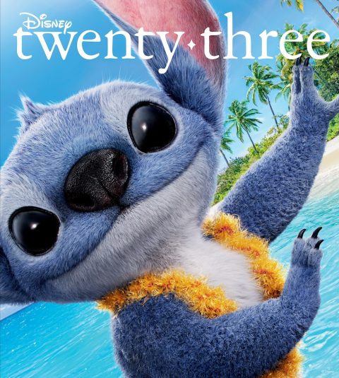 Stitch smiles playfully in a close-up shot on the beach, wearing a fluffy yellow lei, with bright blue ocean water and palm trees in the background. The image is the cover of the Summer 2025 issue of Disney twenty-three.