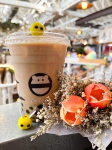 The “Hunny Potion” drink from Mini Monster. It is a blend of creamy honey infused milk tea, served over ice with your choice of boba or lychee jelly (pictured with boba). Inspired by the sweet golden treat loved by a lovable bear. Photographed with prop bees and roses.