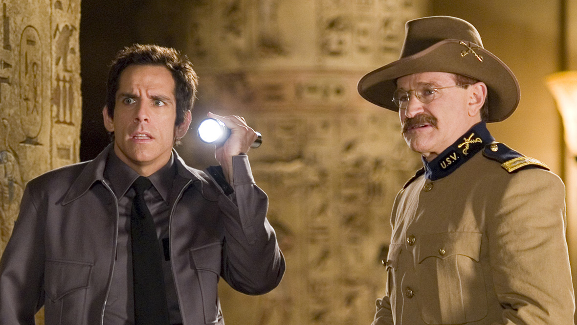 Security guard Larry Daley and Theodore Roosevelt Night at the Museum. Daley is holding a flashlight and wearing a grey security guard uniform. Roosevelt is in a brown military uniform holding a rifle. 