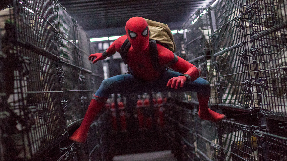 Spider-Man from Spider-Man: Homecoming. He is wearing his superhero suit and a backpack and is standing between two rows of crates.
