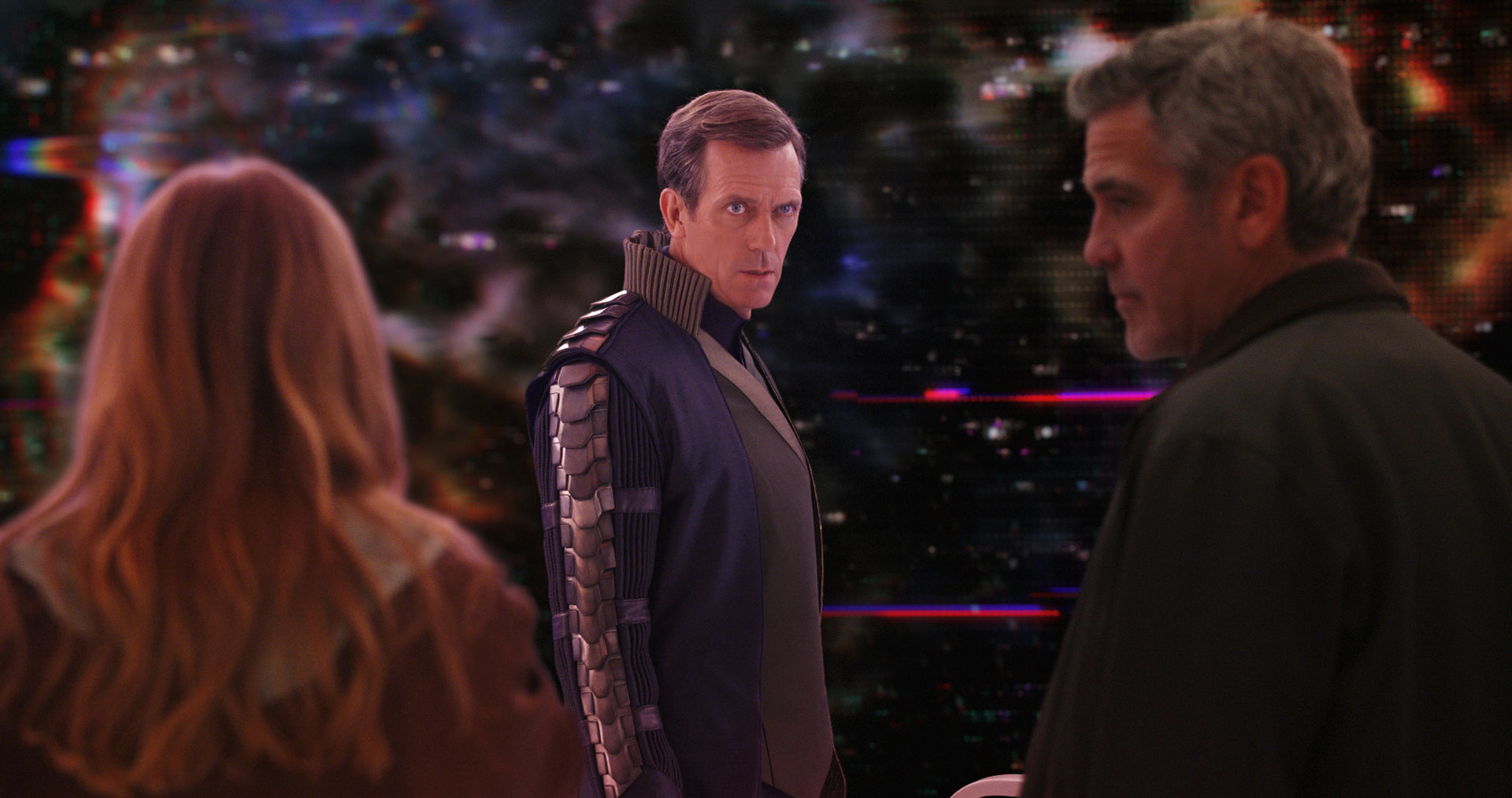 Three characters stand in a futuristic, cosmic setting filled with vibrant lights and digital distortions. In the center, Hugh Laurie portrays Governor Nix, wearing dark, armored attire and staring intently ahead. On the right, George Clooney appears as Frank Walker, partially in profile. Facing them with her back to the camera is Britt Robertson as Casey Newton. 