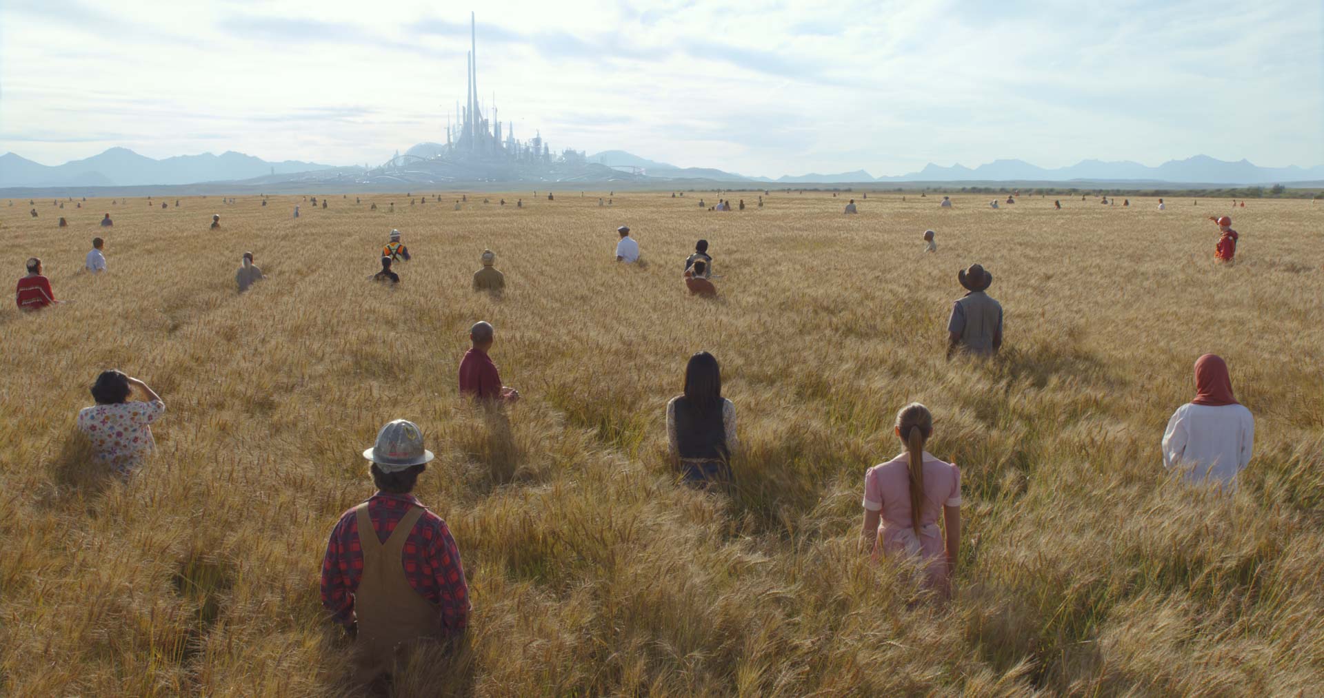 A wide shot from Tomorrowland shows dozens of people standing in a golden wheat field, all facing a gleaming futuristic city on the horizon. The towering cityscape glows under a clear sky, symbolizing hope and progress as people from around the world are drawn toward it. The moment captures the film’s central theme of optimism and imagination.