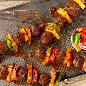 Colorful Hawaiian BBQ skewers featuring golden-brown Impossible® Meatballs, charred pineapple chunks, red bell peppers, and onions, all glazed with a glossy barbecue sauce and served on a wooden board.