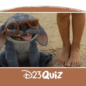 Image from the live-action reimagining of Lilo & Stitch (2025). Stitch is sitting and panting, on a dirt road, wearing a pair of orange glasses made of pipe cleaners. Lilo (Maia Kealoha) standing next to him, walking barefoot.