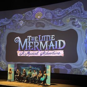 A picture of the stage at D23’s screening event of The Little Mermaid. Onstage is Jodi Benson and a panel of creatives from The Little Mermaid – A Musical Adventure against a backdrop of the new show.