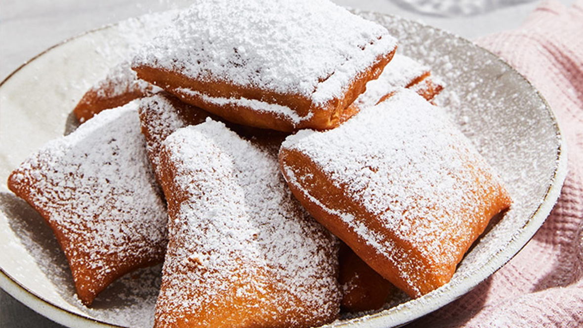Gold Member Offer: 10% Off at Jazz Kitchen Coastal Grill & Patio Multiple browned beignets that look as if they’ve just been popped out of the fryer huddle together and rest on a white plate. Mounds of sprinkled white powdered sugar cover each beignet. Some of the leftover powdered sugar sits at the circumference of the plate.