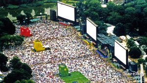 A large crowd of 100,000 guests sit on blankets in front of four large screens in Central Park for the premiere of Pocahontas on June 10, 1995.