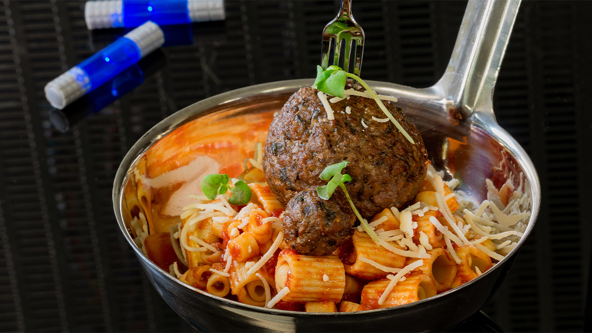 Impossible™ Spoonful previously served at Pym Test Kitchen in Disney California Adventure. The dish features ditalini and rigatoni pasta and two sizes of meatballs tossed in a marinara sauce. The dish is served in a large ladle and a miniature fork and garnished with plant-based Parmesan cheese and microgreens.