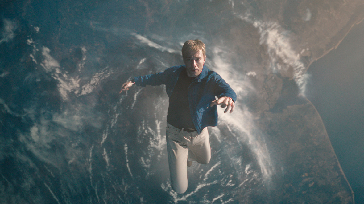 Joseph Quinn as Johnny Storm/Human Torch in Marvel Studios’ The Fantastic Four: First Steps. He is wearing a blue jacket and white pants and is falling from space back down to Earth.