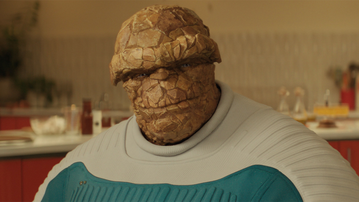 Ebon Moss-Bachrach as Ben Grimm/The Thing in Marvel Studios’ The Fantastic Four: First Steps. He is a creature with tan, rock-like skin. He is wearing a blue and white Super Hero suit.
