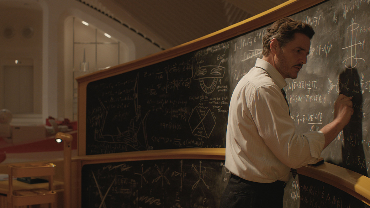 Pedro Pascal as Reed Richards/Mister Fantastic in Marvel Studios’ The Fantastic Four: First Steps. He is wearing a white button-down shirt and doing complex math on a long chalkboard.