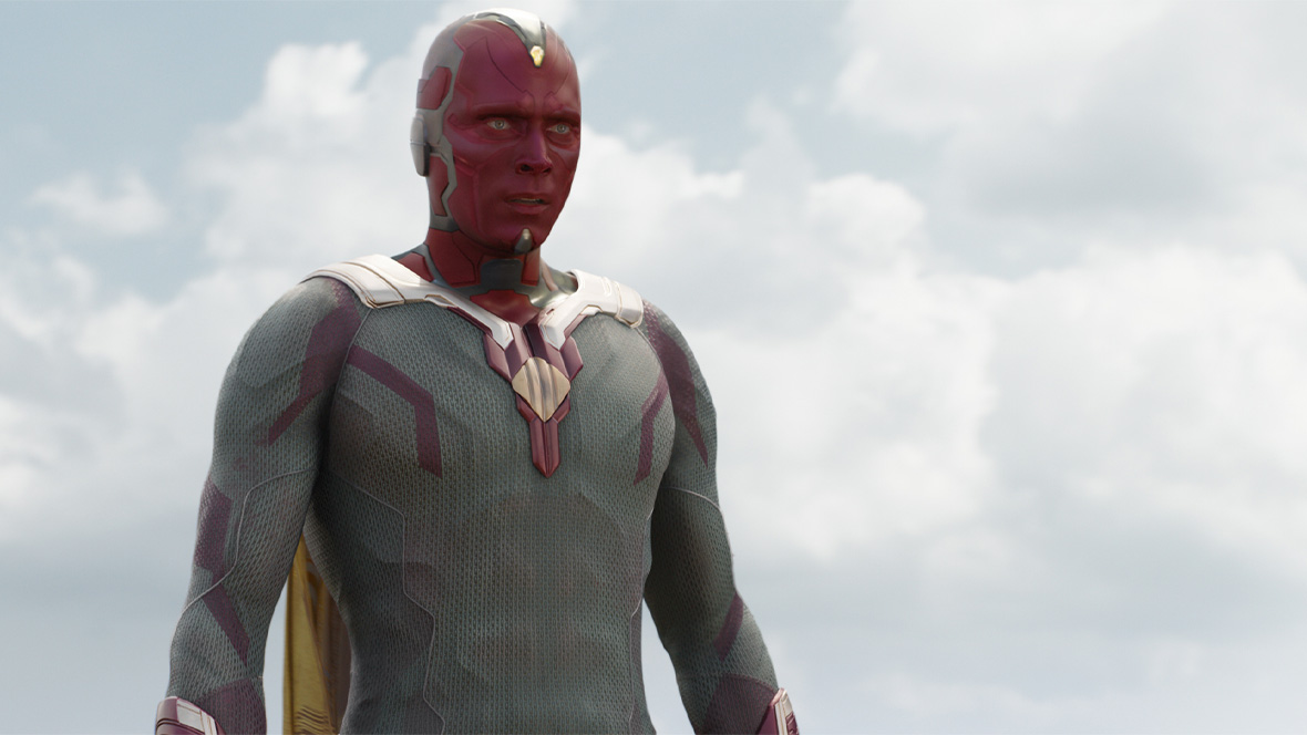 Vision from Captain America: Civil War (2016) wearing his gray and red Super Hero suit and floating in the sky with gray clouds behind him.