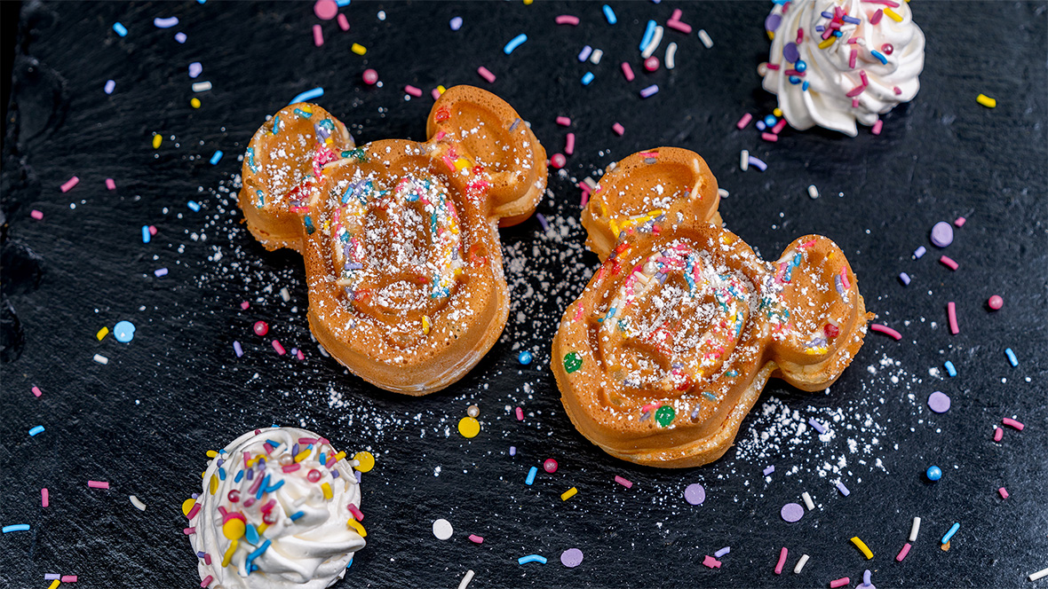 Two Mickey Mouse-shaped waffles, topped with powdered sugar and rainbow sprinkles