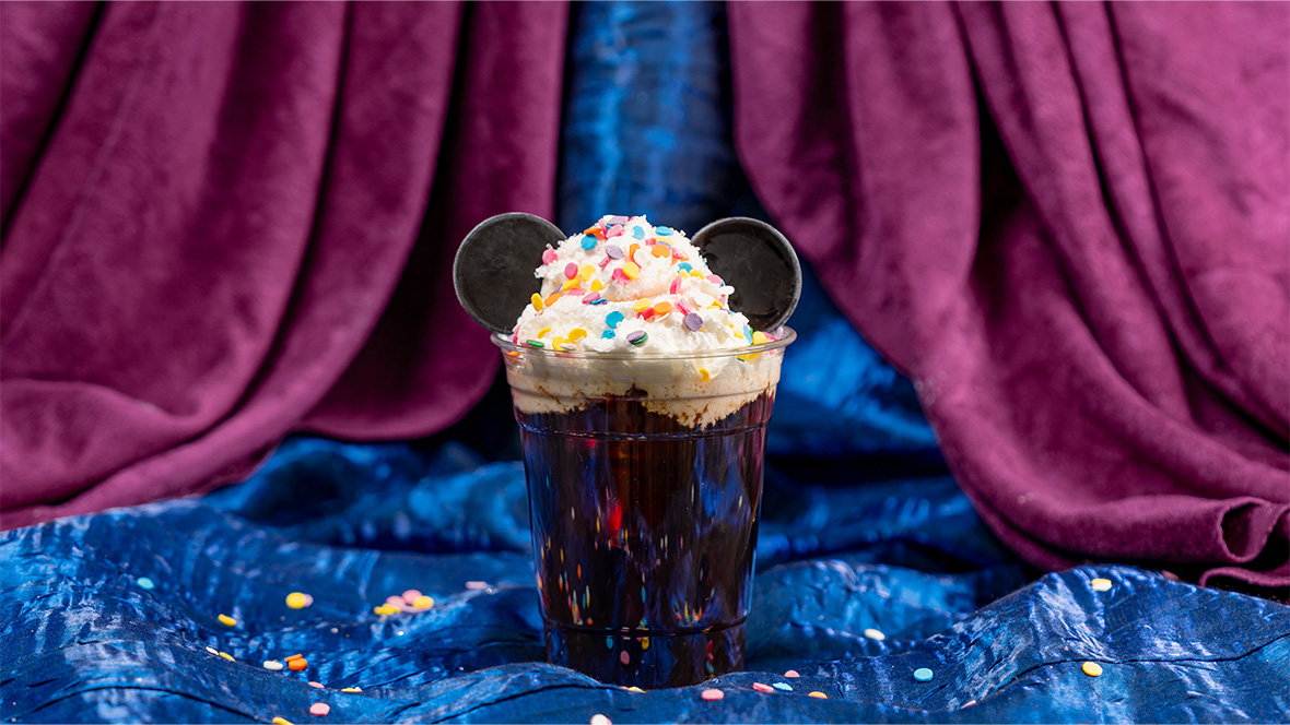 Cold brew coffee at Café Daisy at Disneyland Resort, topped with whipped cream, round rainbow sprinkles, and two chocolate medallions that looks like Mickey Mouse’s ears