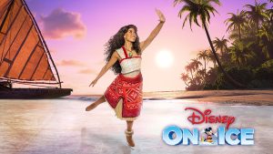 An ice skater dressed as Moana glides along the ice with her hand in the air. The background is a beach setting complete with a shoreline, palm trees, and a sunset turning the sky a purplish-orange hue. In the far background is Moana’s immediately recognizable boat.